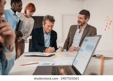 Senior executive signing a contract with a multigenerational team observing, in a collaborative office environment. - Powered by Shutterstock