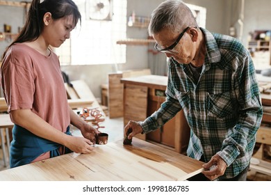 Senior experienced carpenter showing aprentice how to cover wooden board with lacquer to protect it and give shine - Powered by Shutterstock