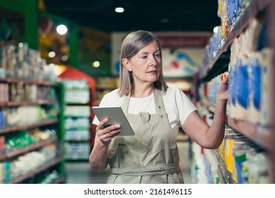 Senior experienced female employee of the store conducts an inventory of goods, uses a tablet computer - Powered by Shutterstock