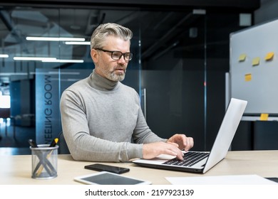 Senior And Experienced Programmer Works In Modern Office At Laptop, Male Web Designer Developer In Glasses Writes Code Programs New Application, Mature Businessman Works At Desk.