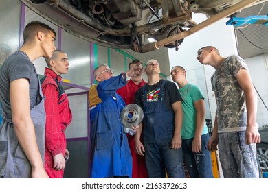Senior experienced teacher standing underneath car on hydraulic ramp and teaching automotive trade to his students in the vocational school - Shutterstock ID 2163372613