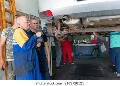 Senior Experienced Teacher Standing Underneath Car On Hydraulic Ramp And Teaching Automotive Trade To His Students In The Vocational School