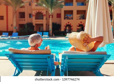 Senior Family Couple Relaxing By Swimming Pool Lying On Chaise-longues. People Enjoying Summer Vacation.