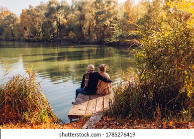 Senior family couple relaxing by autumn lake. Man and woman enjoying nature and hugging sitting on pier - Powered by Shutterstock