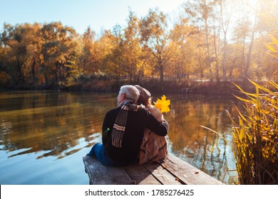 Senior family couple relaxing by autumn lake. Man and woman enjoying nature and hugging sitting on pier