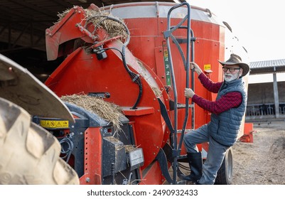 Senior farmer climbing ladder on agriculture device for cow feed mixture - Powered by Shutterstock