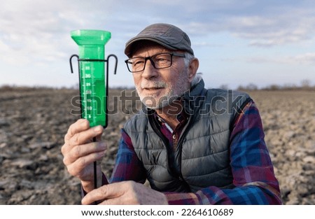Senior farmer looking at water gauge for rain measuring in field