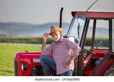 Senior farmer with straw hat standing beside small tractor in field - Powered by Shutterstock