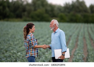 Senior farmer and young woman shaking hands on field