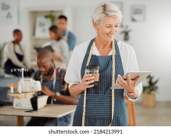 Senior Fashion Designer Reading Online Orders From A Handheld Tablet Inside Her Shop. Old Female Clothing Producer Smiling About Her Success While Holding Coffee. A Happy Mature Creative