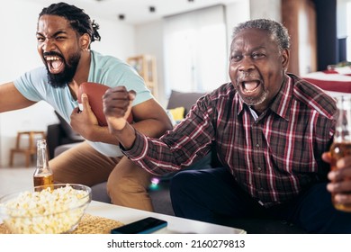 Senior father and adult son cheering for american football game at home - Powered by Shutterstock