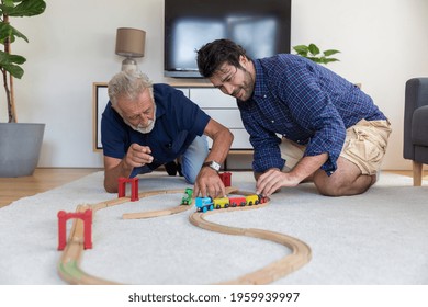 Senior Father And Adult Son Playing With Toy Wooden Together At Home With Happy And Smile. Two Men Playing With Toy Car On Floor In Living Room