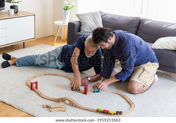 Senior father and adult son playing with toy wooden\
together at home with happy and smile. Two men playing with toy car\
on floor in living room