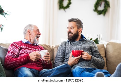 A Senior Father And Adult Son Sitting On A Sofa At Home At Christmas Time, Talking.