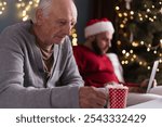 Senior father sits quietly, feeling isolated as his son focuses on work during Christmas. The old man, with a sense of solitude, holds his drink