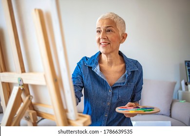 Senior Female Artist Working On Painting. Elderly woman painting on a canvas seated on a chair at home. Senior woman painting on canvas. Art school, creativity and people concept - Powered by Shutterstock