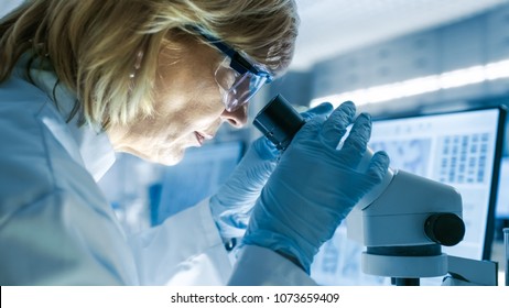Senior Female Biologist Works on Her Computer and Looks at Materials under Microscope. She's in a Modern Laboratory.