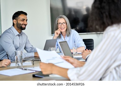 Senior female ceo and happy multicultural business people discussing company presentation at boardroom table. Smiling diverse corporate team working together in modern meeting room office.