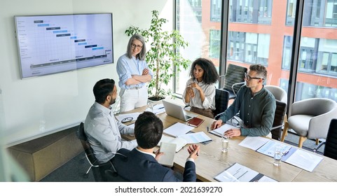 Senior female ceo   multicultural business people discussing company presentation at boardroom table  Diverse corporate team working together in modern meeting room office  Top view through glass