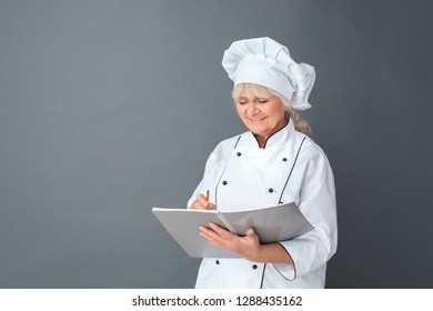 Senior Female Chef Studio Standing Isolated On Gray Wall Writing Working Process In Journal Smiling Joyful