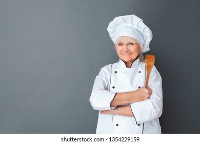 Senior Female Chef Studio Standing Isolated On Gray Wall Holding Wooden Spatula Crossed Arms Looking Camera Smiling Happy