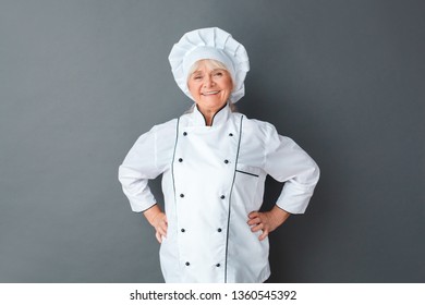 Senior Female Chef Studio Standing Isolated On Gray Wall Hands On Hips Looking Camera Smiing Cheerful