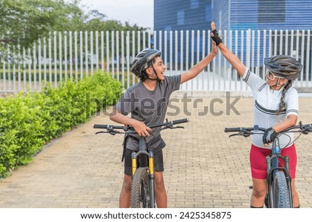 A senior female cyclist and a young male cyclist share a high five, celebrating a joyful moment during their bike ride.