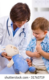 Senior Female Doctor And Happy Child Examining Teddy Bear.