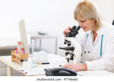 Senior female doctor looking in microscope at laboratory