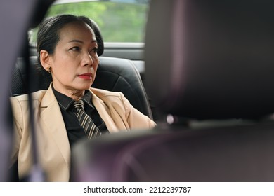 Senior Female Executive Manager Traveling To Office By A Luxurious Car Sitting On Backseat.