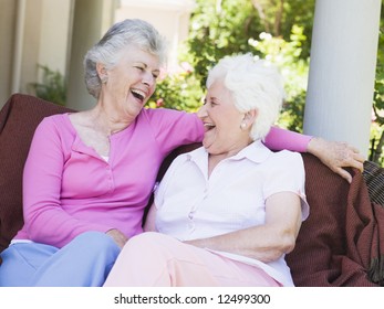 Senior Female Friends Laughing Together Sitting On Garden Seat