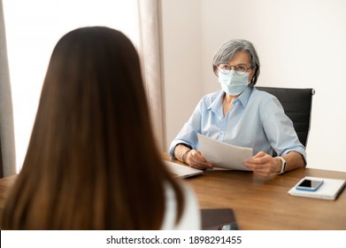 Senior Female Hr Manager Sitting At The Office, Wearing Face Mask, Training Young Female Worker Intern, Interviewing Job Seeker, Checking Cv, Mentoring Student. Social Distance And Safety Concept