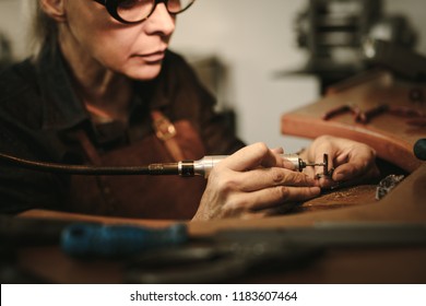 Senior Female Jewelry Maker Polishing A Product At Her Workbench. Jewelry Designer Polishing A Bracelet At Workshop.