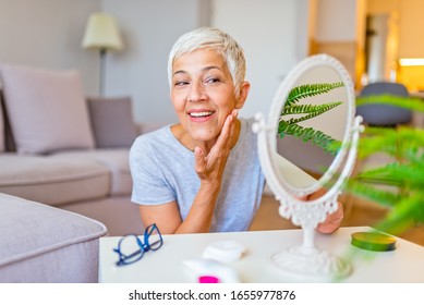 Senior Female Looking At Sagging Skin Face In Mirror, Old Age Appearance. Portrait Of Senior Woman Applying Anti-aging Cream. Portrait Of An Attractive Middle Aged Woman Looking Into A Mirror