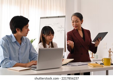 Senior Female Manger Discussing Business Plan Marketing Strategy With Young Worker At Modern Corporate Office