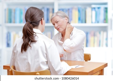 Senior Female Patient Consulting Her Physician Or Doctor On Account Of Chronic Neck Pain Caused By Fibromyalgia, Osteoporosis Or A Herniated Disc.