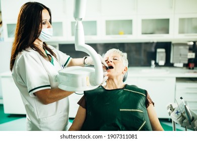 Senior Female Patient On A Dentist Appointment. Regular Check Up At Orthodontist. Specialist Examining A Older Patient. Dental Prosthetics Implant For Retired Pensioner Woman.Dentist Wearing A Mask