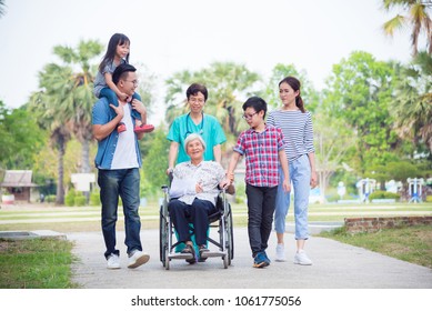 Senior female patient sitting on wheelchair with her family and nurse in hospital park