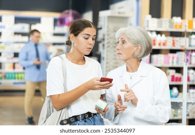 Senior female pharmacist talk to girl buyer and help to scan QR code on package, find out information about medical cosmetics. Specialist in pharmacy answer buyers question, consulting services - Powered by Shutterstock