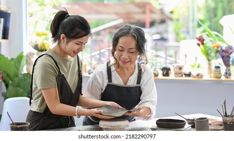 Senior Female Potter Teaching Young Woman Creating And Sculpting Clay Pot In Craft Studio Workshop