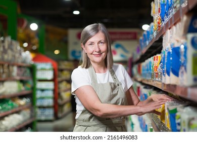 Senior female supermarket worker lays out the goods on the shelves - Powered by Shutterstock