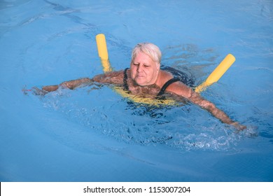 A senior female woman holds on to a flotation device on a swimming pool to learn how to swim - Powered by Shutterstock