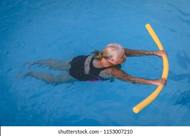 A senior female woman holds on to a flotation device on a swimming pool to learn how to swim - Powered by Shutterstock