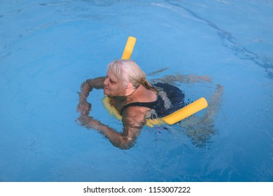 A senior female woman holds on to a flotation device on a swimming pool to learn how to swim - Powered by Shutterstock