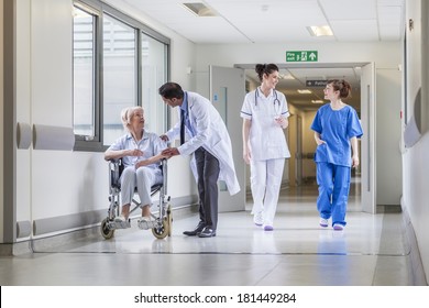 Senior female woman patient in wheelchair sitting in hospital corridor with Asian Indian male doctor and female nurse colleagues