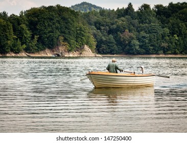 Senior fisherman rowing in a boat on a lake - Powered by Shutterstock