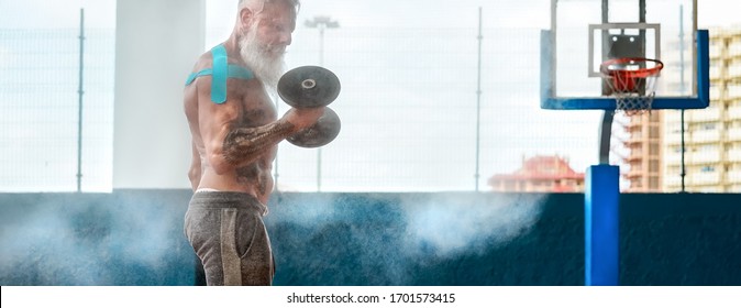 Senior Fitness Man Doing Biceps Curl Exercises Inside Old Gym - Fit Mature Male Training With Dumbbells In Wellness Club Center - Body Building And Sport Healthy Lifestyle Concept