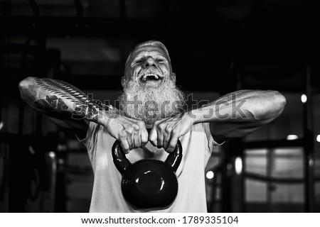 Senior fitness man doing kettle bell exercises inside gym - Fit mature male training in wellness club center - Body building and sport healthy lifestyle concept - Black and white editing