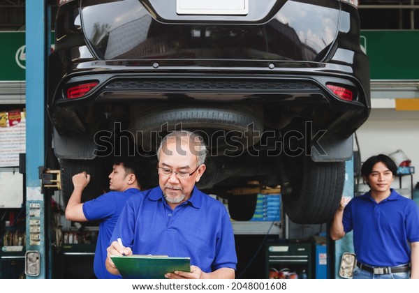 Senior foreman checking list of vehicle repair service\
while two mechanic checking wheel, inspecting under car body of\
customer car at automobile garage service, vehicle repair service\
shop concept. 