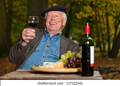 Senior French Man Enjoying Red Wine And Cheese Outdoors In Autumn Forest.